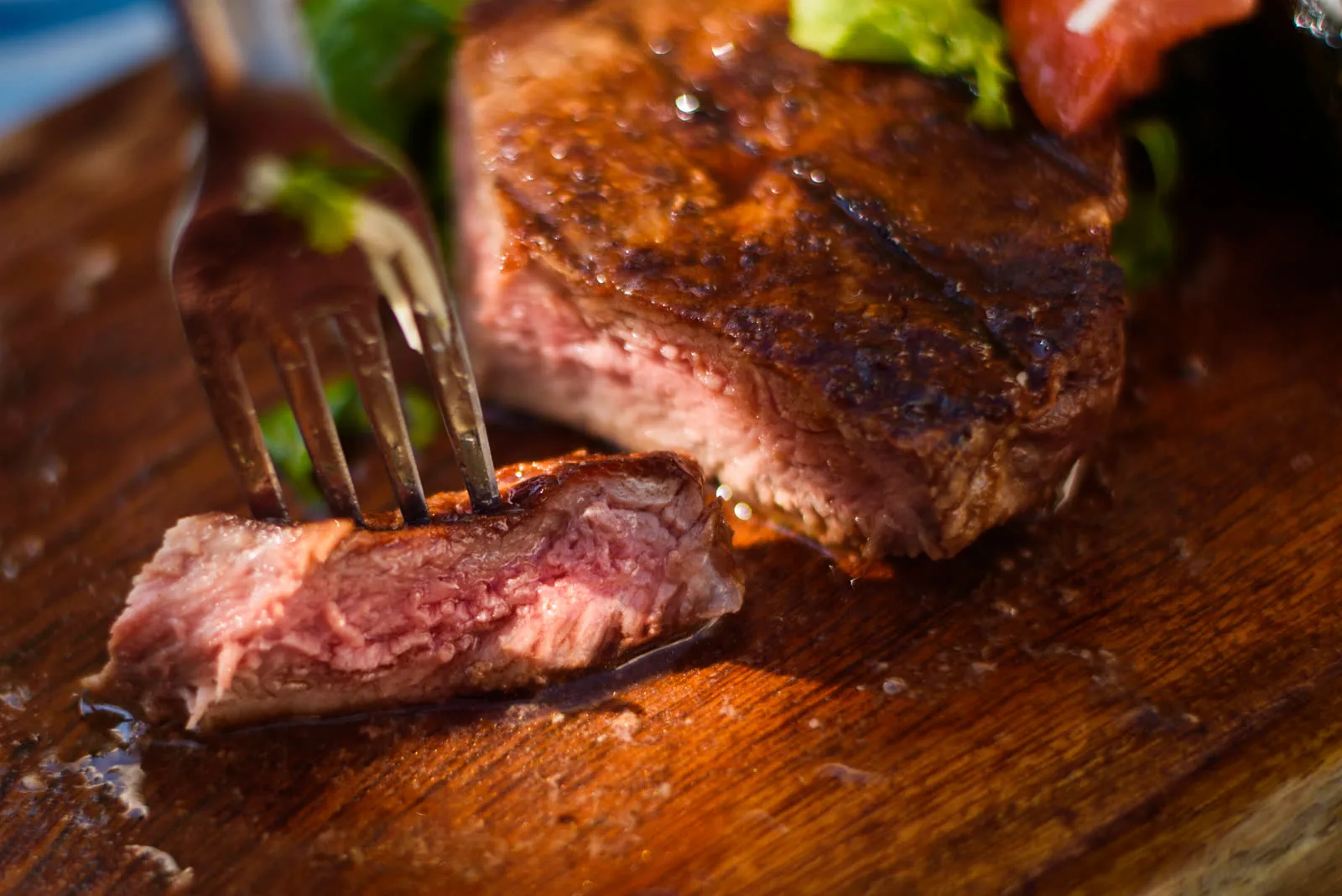 Bife de chorizo a la parrilla cortado al medio, con el punto jugoso rosado a la vista, sobre una tabla de madera